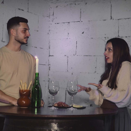 Pareja charlando en una mesa con botellas de vino y copas, en un ambiente contemporáneo y acogedor.